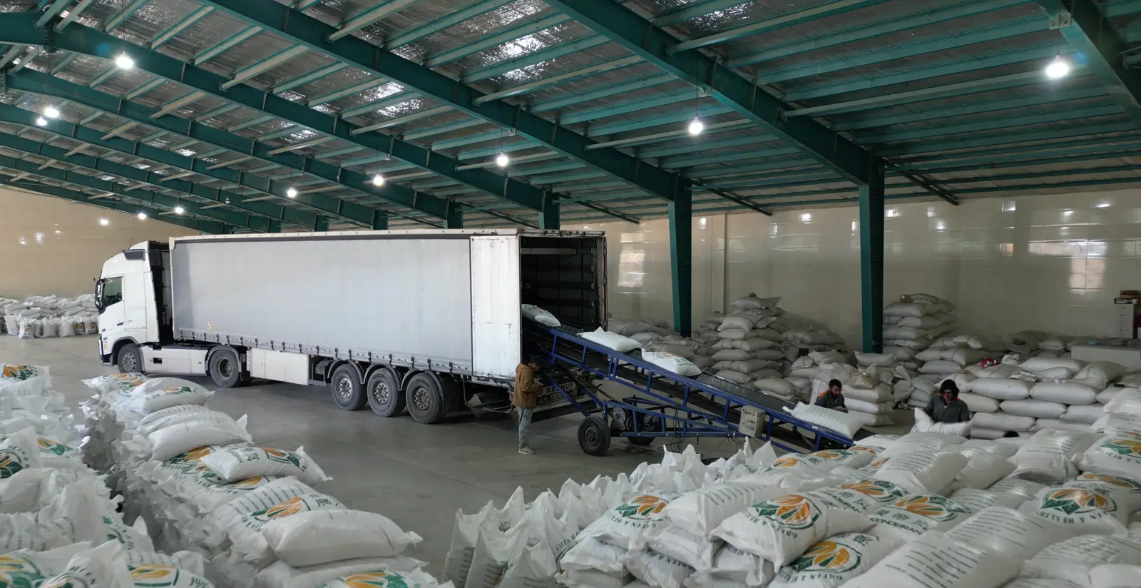 Warehouse full of pistachio bags, a truck being loaded by conveyor